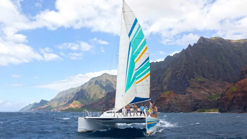 Sailing catamaran under sail along the cliffs on a Na Pali Coast boat tour from Port Allen, Kauai