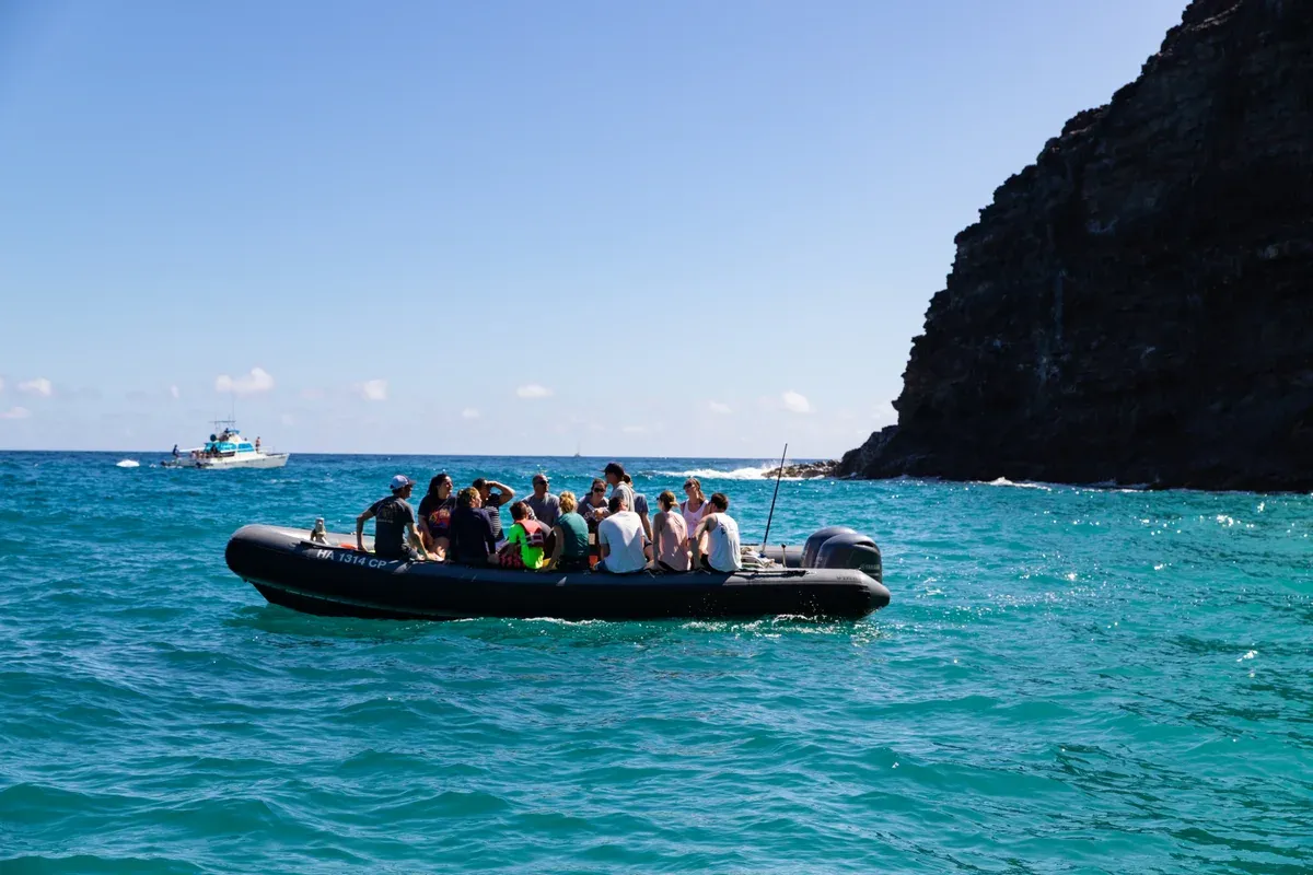 Zodiac raft carrying passengers below a sea cliff on a Na Pali Coast raft tour, Kauai