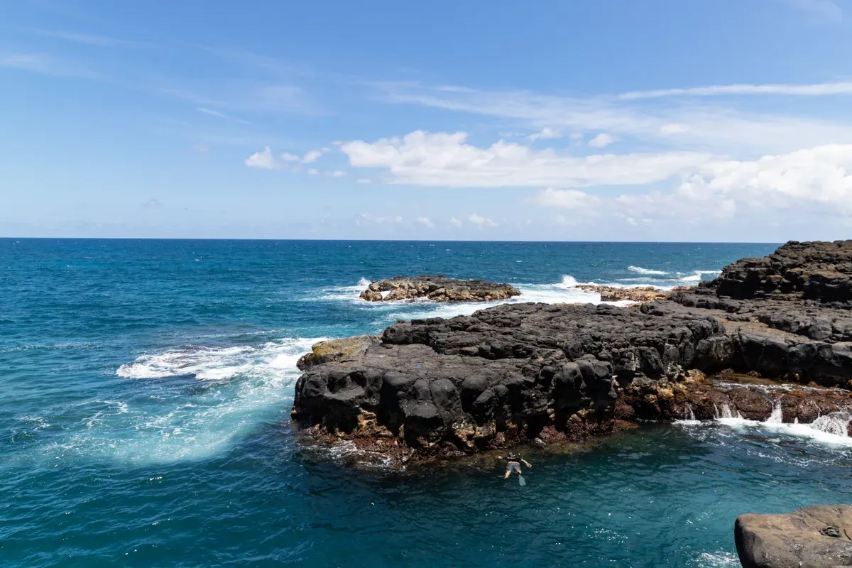 Snorkeler near the lava rocks of Queen's Bath on Kauai, like Na Pali Coast snorkel tours