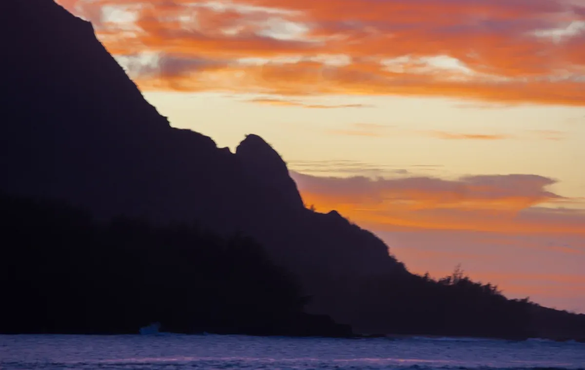 Orange sky behind a dark Kauai headland at sunset on Napali Coast sunset cruises